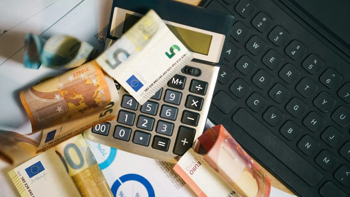 Calculadora y billetes de euro junto a documentos, representando el cálculo de impuestos
